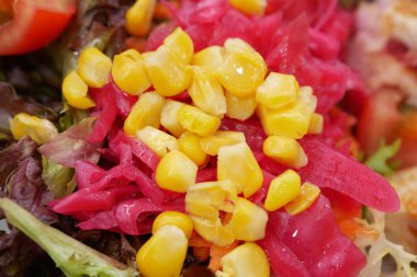 Canlı bir salata, turşulu pembe sebzeler ve tatlı mısır, görsel olarak çekici ve lezzetli.