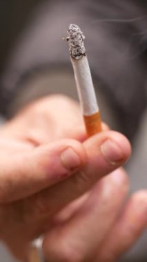 Bir el, havada yükselen dumanı üreten yanan bir sigarayı sıkıca kavrıyor.
