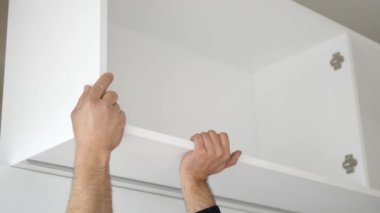 Bir birey dikkatli bir şekilde modern bir mutfak alanında parlak beyaz bir dolap rafı kuruyor.