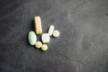 Çeşitli renkli ve çeşitli haplar ve tabletler dikkatlice karanlık bir yüzeye yerleştirilmiş.