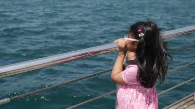 Bir kız denizin kenarında durur, ufka doğru nefes kesici okyanus manzarasına hayran kalır.