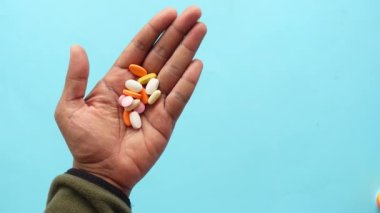 Bir el, yumuşak mavi arka planda çeşitli renkli hapları tutarken görülüyor.