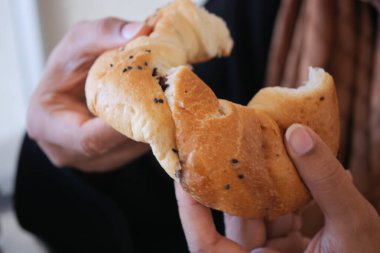 Lezzetli siyah tohumlarla kaplı bir parça taze ekmeği nazikçe parçalayan bir insan.