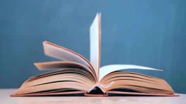 Yeşil bir arka plana karşı ahşap bir masa üzerinde sayfaları dönen açık bir kitap.