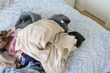 Çeşitli giysiler bir yatağa saçılmış, canlı ve renkli bir çamaşır sahnesi yaratıyor.