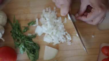 Eller ustalıkla doğranmış soğan ve çeşitli taze otları ahşap kesme tahtasında hazırlıyor.