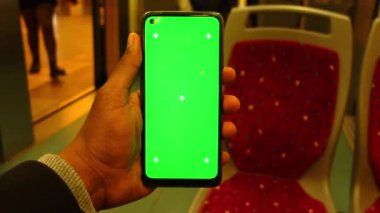 Trenin içinde yeşil ekranlı akıllı telefon kullanan genç adam. ,