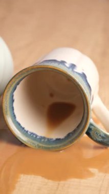 Tepetaklak olmuş bir seramik bardak, üzerine kahve dökülmüş ahşap bir masada oturur.