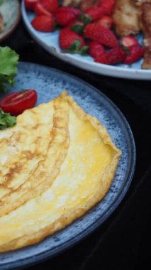Çok güzel pişirilmiş, mükemmel altın bir omlet, canlı turuncu bir tabakta servis edilir.