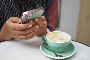 Sıcak bir kahve fincanını yudumlarken tesadüfen telefonuna bakan bir insanın samimi anı.