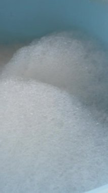 Yüzeyde, sabunlu suyla dolu mavi bir havuzda yüzen köpüklü baloncukların yakın çekim görüntüsü.