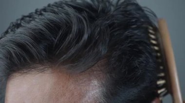 Bu resim, birinin saçını ahşap bir fırçayla dikkatlice taramasını gösteriyor.
