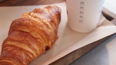 Lezzetli bir kruvasan, ahşap bir yüzeyde dumanı tüten bir kahveyle mükemmel bir şekilde eşleştirilir.