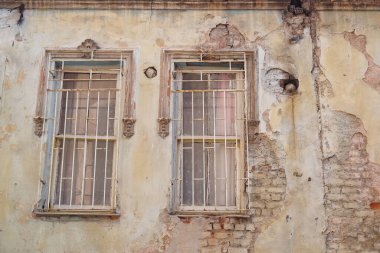 Çürümüş bir duvardaki boyaların ve parmaklıklı pencerelerin yakınlaşması cesur dokuları ortaya çıkarıyor.