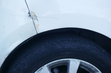 Beyaz bir arabanın çamurluğunda, özellikle lastik alanının yakınında görülebilen bir hasar var.