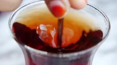 Bir el şeffaf ve berrak bir cam kabın içinde ılık bir içeceği nazikçe karıştırıyor.