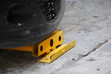 Close-Up of Car Wheel Secured with Yellow Wheel Clamp on Pavement. clipart