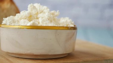 Kremalı ricotta peyniri yumuşak ahşap bir arka planda kırsal bir kasede zarif bir şekilde sergilenir.