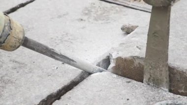 İki işçi inşaat alanındaki beton levhaları kaldırmak için matkap ve aletler kullanıyor..