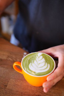Nefis bir yeşil latte, sanatsal olarak sersemletici bir turuncu fincanda sunuluyor.