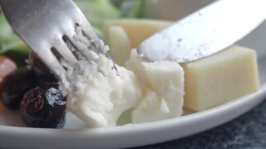 Lezzetli bir tat için çeşitli zeytinler ve taze yeşillikler içeren bir peynir tabağı.