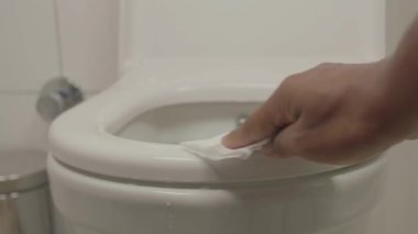 Birisi tuvalet kenarlarını titizlikle temizlemek için temizleme bezi kullanıyor.