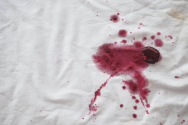Canlı ve zengin bir kırmızı şarap sızıntısı el değmemiş beyaz bir kumaşta göz alıcı bir leke oluşturur.