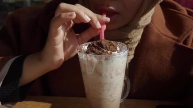 Krem şanti ve süslemelerle kaplı kremalı çikolatalı milkshake yudumlamayı seven bir insan.