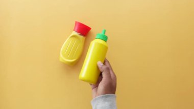 Bir el, sarı hardal şişelerini dikkatlice parlak ve canlı sarı bir yüzeye yerleştiriyor.