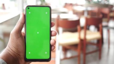 Kafede boş yeşil ekranlı bir telefonu tutan el.