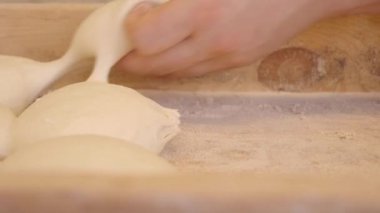 Becerikli bir fırıncı ustalıkla el yapar taze, yumuşak hamur kalıplarını iyi giyimli ahşap bir yüzeye döker