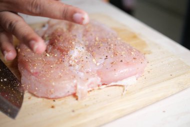 Yetenekli bir şef, mutfaktaki tahta kesme tahtasıyla çiğ tavuk göğsünü ustalıkla dilimliyor.