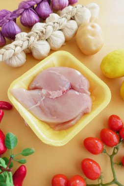 Çiğ tavuk parçaları taze sebzelerle ve tabağı geliştiren aromatik otlarla çevrilidir.