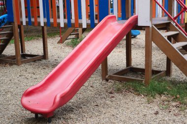 A vibrant and bright red slide positioned within a childrens play area filled with gravel clipart