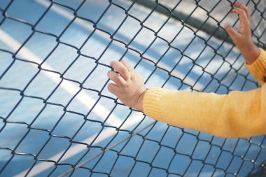 Meraklı bir çocuk tenis kortunun çitlerine dokunmak için uzanır ve canlı bir sahne yaratır.