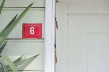 Closeup of house number 6 next to a pristine white door and vibrant lush greenery clipart