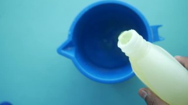 Şişeden mavi konteynıra dökülen sarı sıvının yakın görüntüsü, mutfak aletleri kullanılıyor
