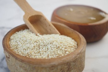 Kırsal ahşap bir kase ve kaşıkta beyaz susam tohumlarına yakın plan, arka planda kırmızı bir kumaş var..