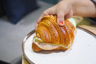 Bir el lezzetli kruvasan sandviçi tutuyor. İçi lezzetli malzemelerle dolu.