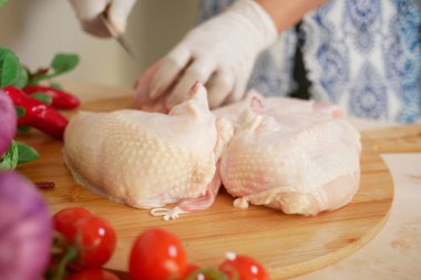 Carefully preparing fresh chicken alongside a variety of vegetables on a wooden cutting board clipart