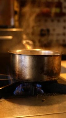 Gaz sobasında kaynayan paslanmaz çelik bir kap, sıcak bir mutfak atmosferi yaratır..