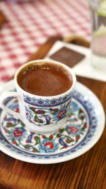 Geleneksel bir çiçekli fincanda servis edilen dumanı tüten Türk kahvesi kareli bir masa örtüsü. Kültürel, aşçılık ve ev temalı projeler için mükemmel..