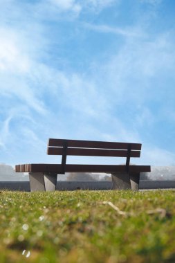Sakin bir ahşap bank, berrak mavi gökyüzünün altındaki yemyeşil çimlerde oturur. Rahatlamak için ideal.