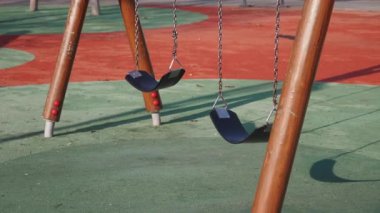 İki boş salıncak canlı, renkli bir oyun sahasında sessizce oturur ve çocukları bekler.
