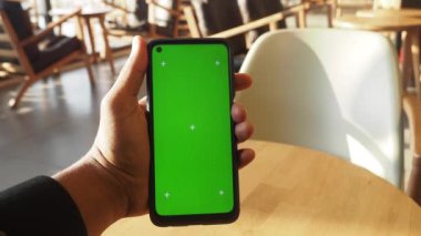 Bir el, kapalı bir ortamda canlı yeşil bir ekran gösteren akıllı bir telefonu tutuyor.