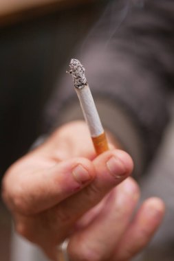 Bir el, havada yükselen dumanı üreten yanan bir sigarayı sıkıca kavrıyor.