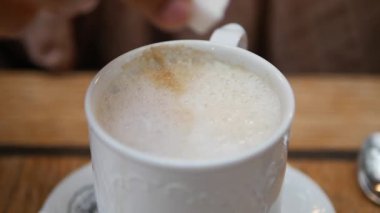 Bir el nazikçe bir küp şekeri dumanı tüten bir fincan kahvenin üzerinde tutuyor.