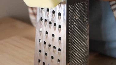 Taze rendelenmiş peynir ahşap bir yüzeyde duran metal rendesinin yanına güzelce istiflenmiş.