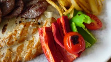 Canlı bir tabak ızgara et, renkli sebzeler ve yanında kızarmış patates.