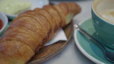 Nefis bir kruvasan, kahve ile servis edilen şık bir kafe masasında.
